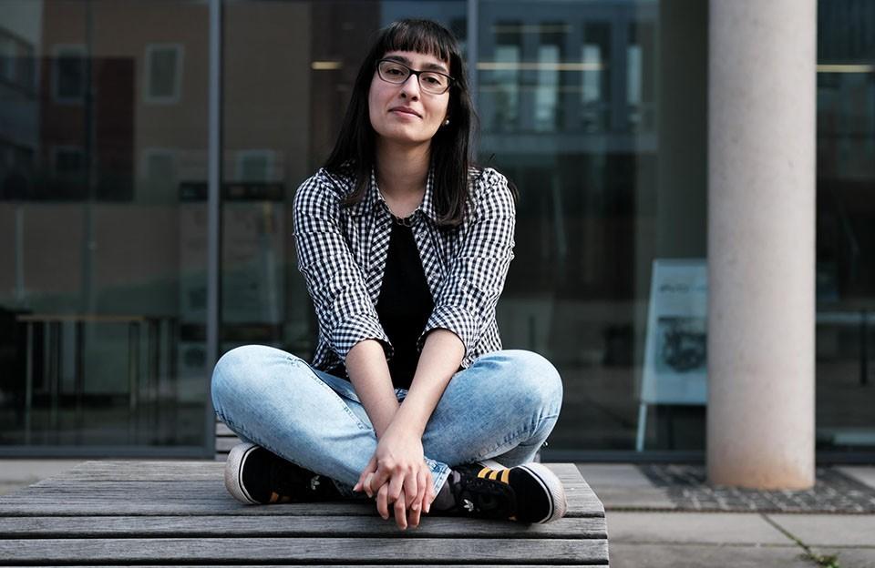 Pardis Bayenat sitzt im Schneidersitz auf einer Bank