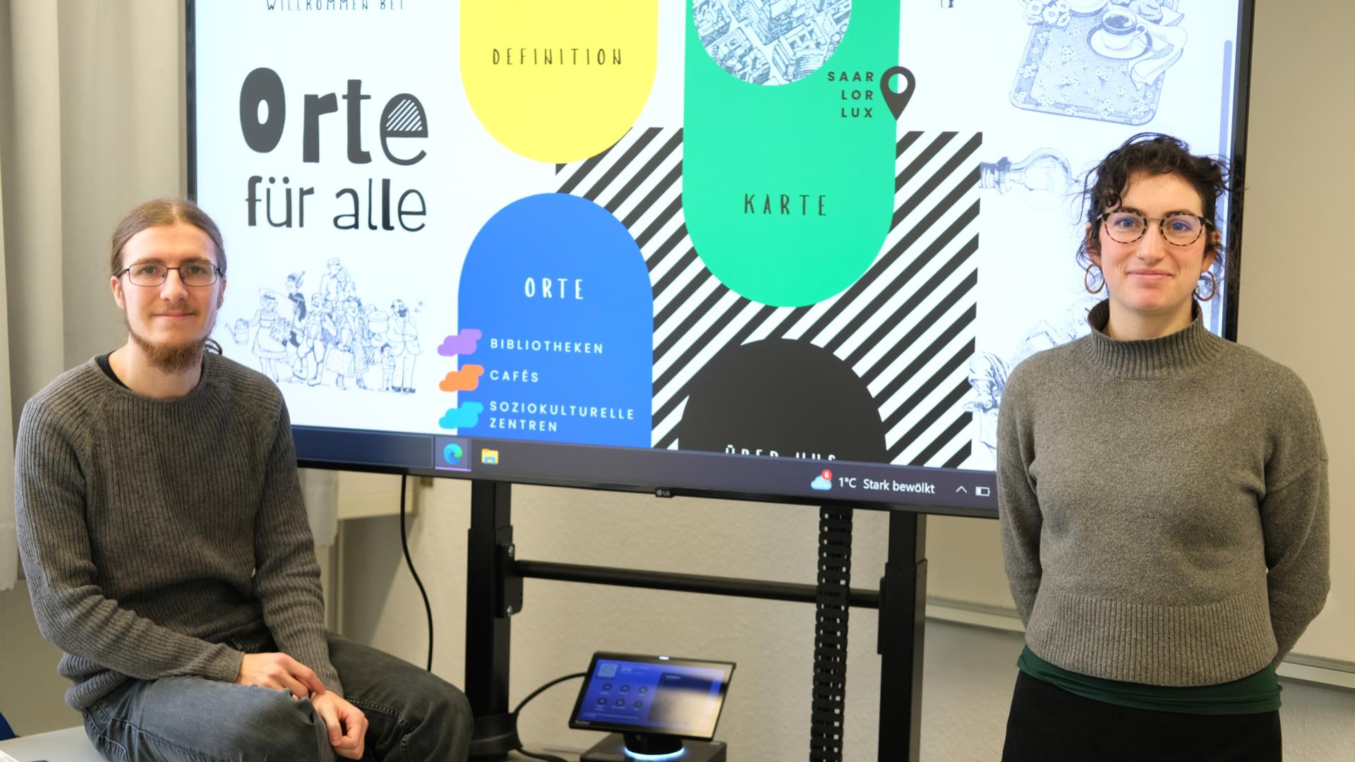 Jan Bentz und Leah Rajchlin vor einem Bildschirm, der ihre Projektarbeit und ihre Plattform vorstellt.