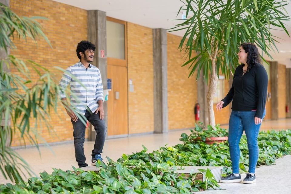 Sakthi Chandrasekaran und Ariana García Lozada stehen sich in einem Gebäude der Universität gegenüber.