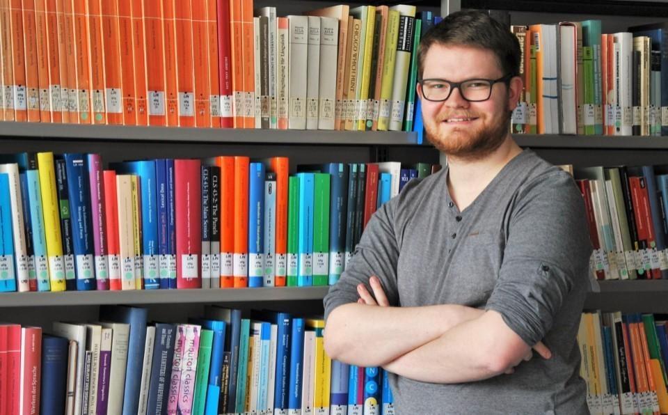 Paul Weis steht vor einem Bücherregal in der Bibliothek