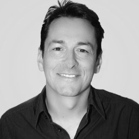 Schwarz-weißes Porträtbild von einem lächelnden Mann mit kurzen schwarzen Haaren und einem dunklen Hemd.