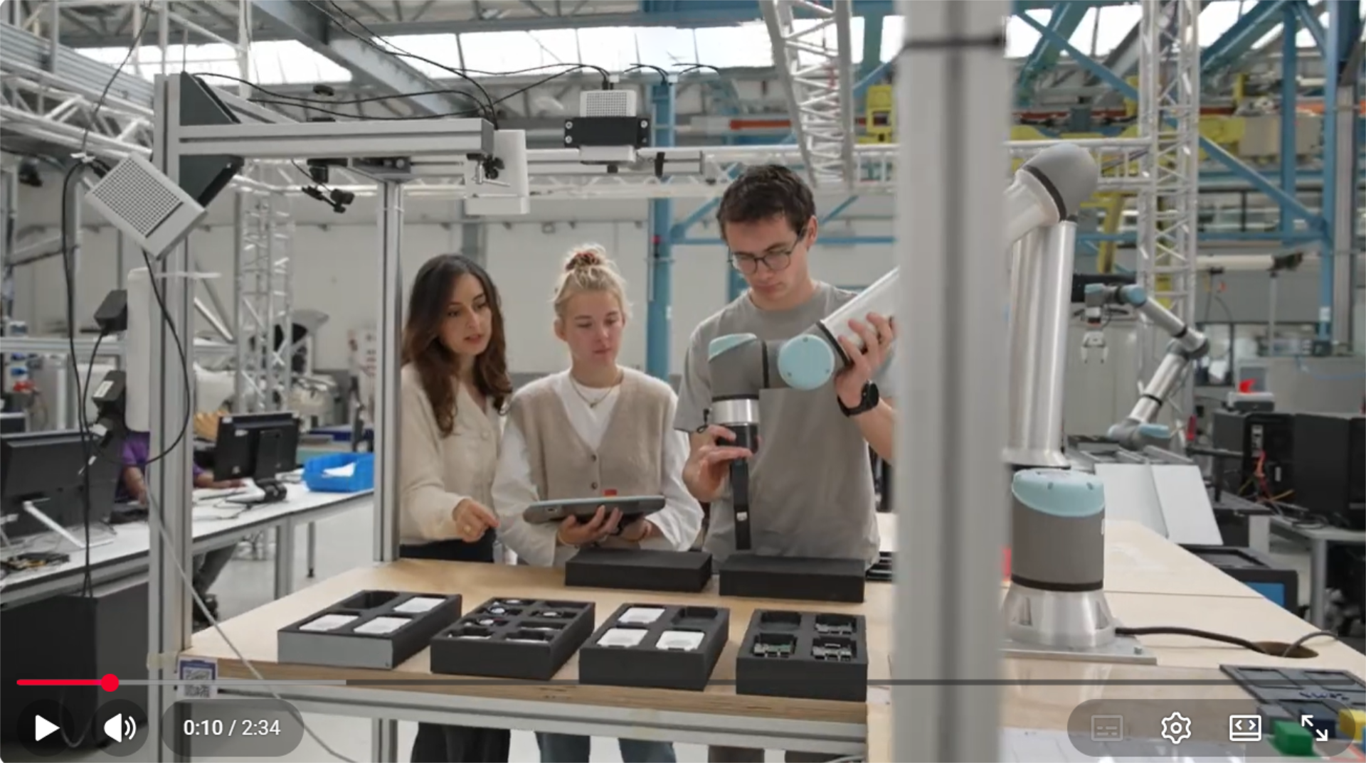 Zwei Studierende mit Dozentin an Roboterarm