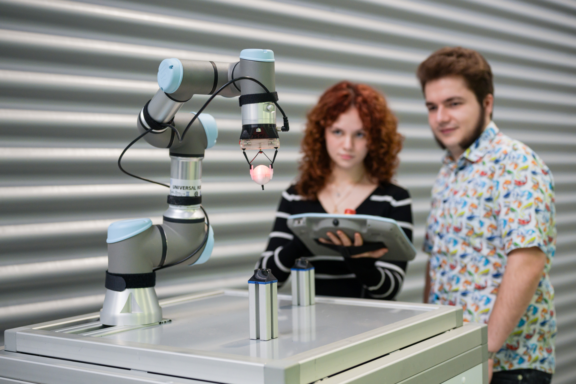 Zwei Studierende hinter einem Roboterarm