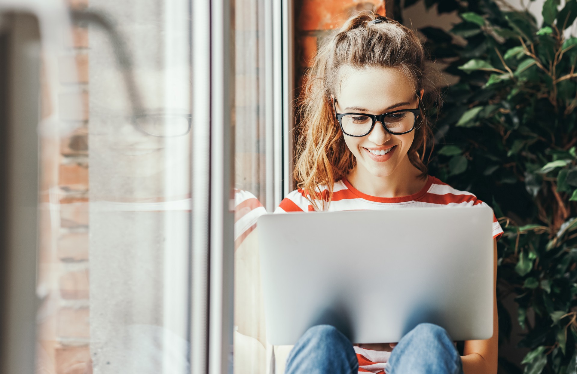 Eine junge Frau mit Brille schaut auf ihr Laptop und lacht.