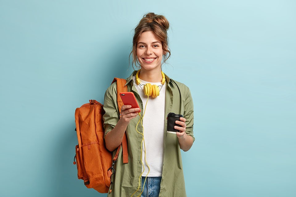 Lachende Studentin mit Handy und Kaffee to go