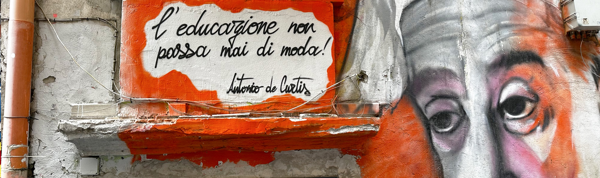 Graffiti auf einer Steinwand mit einem zitat von Antonio de Curtis: "l'educazione non passa mai di moda."