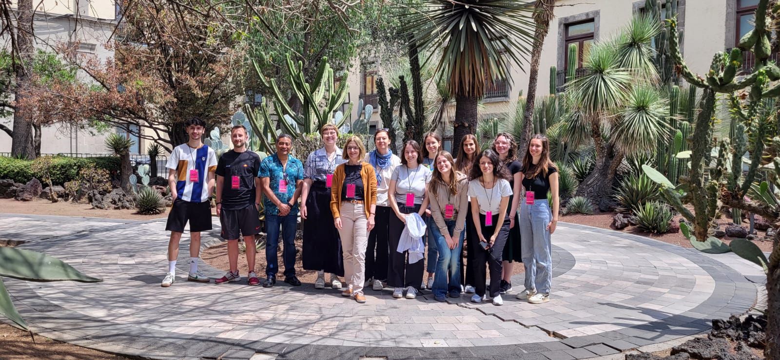 Foto von vielen Menschen nebeneinander auf Steinboden vor einem Palmengarten.