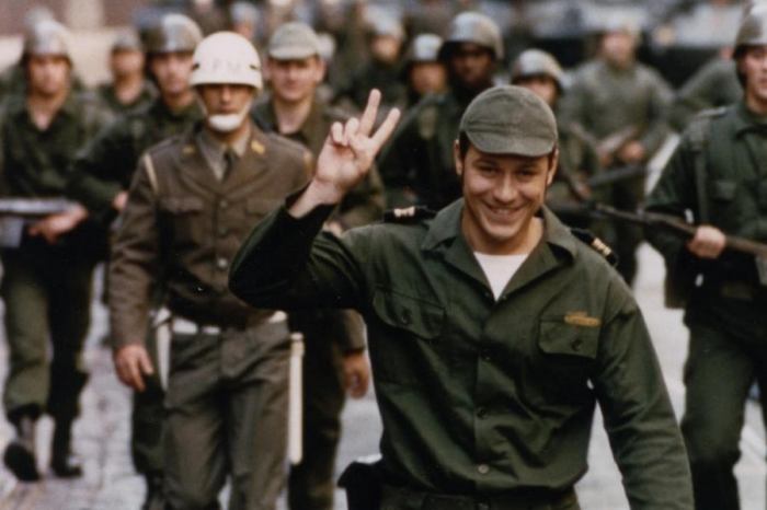 Ein Soldat drückt seine Freude vor der Kamera. Im Hintergrund andere Personen mit Uniform.
