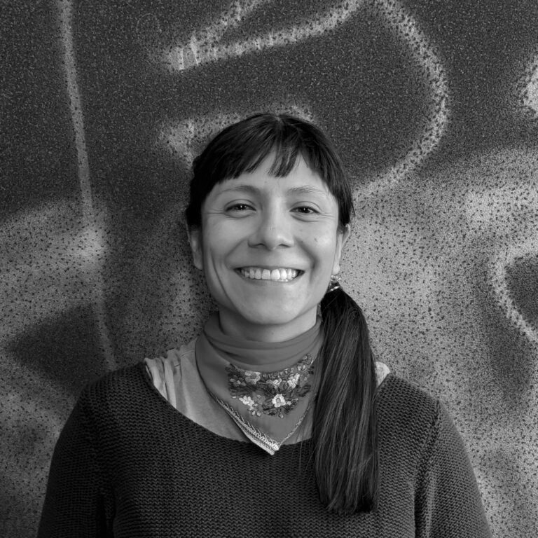 schwarz-weiß Portrait einer Person mit langen dunklen Haaren und einem dunklen Pullover vor einem Grafitti-Hintergrund