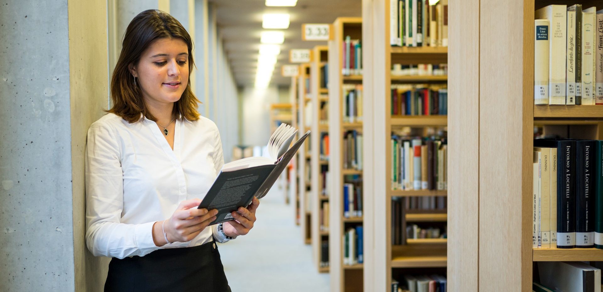 lesende Studentin neben einem Bücherregal