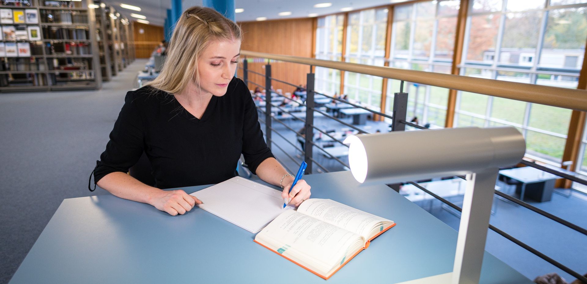 Studentin arbeitet am Schreibtisch in einer Bibliothek