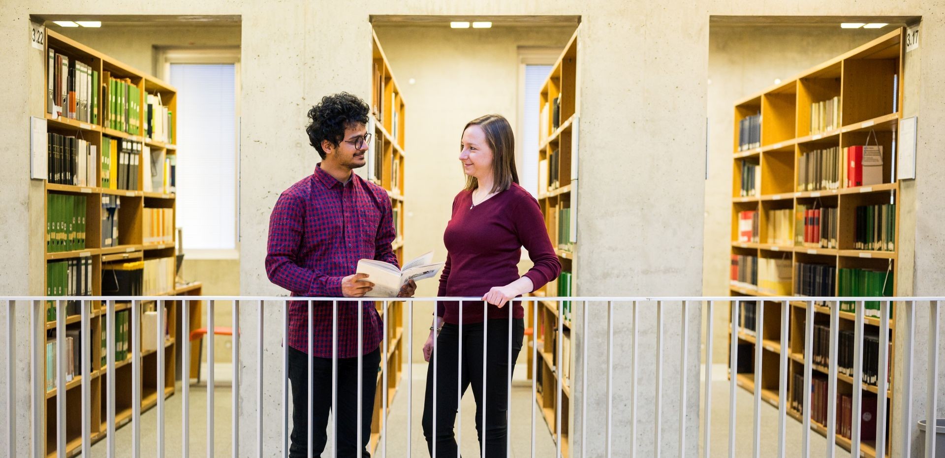 Zwei Studierende lächeln sich in der Bibliothek an