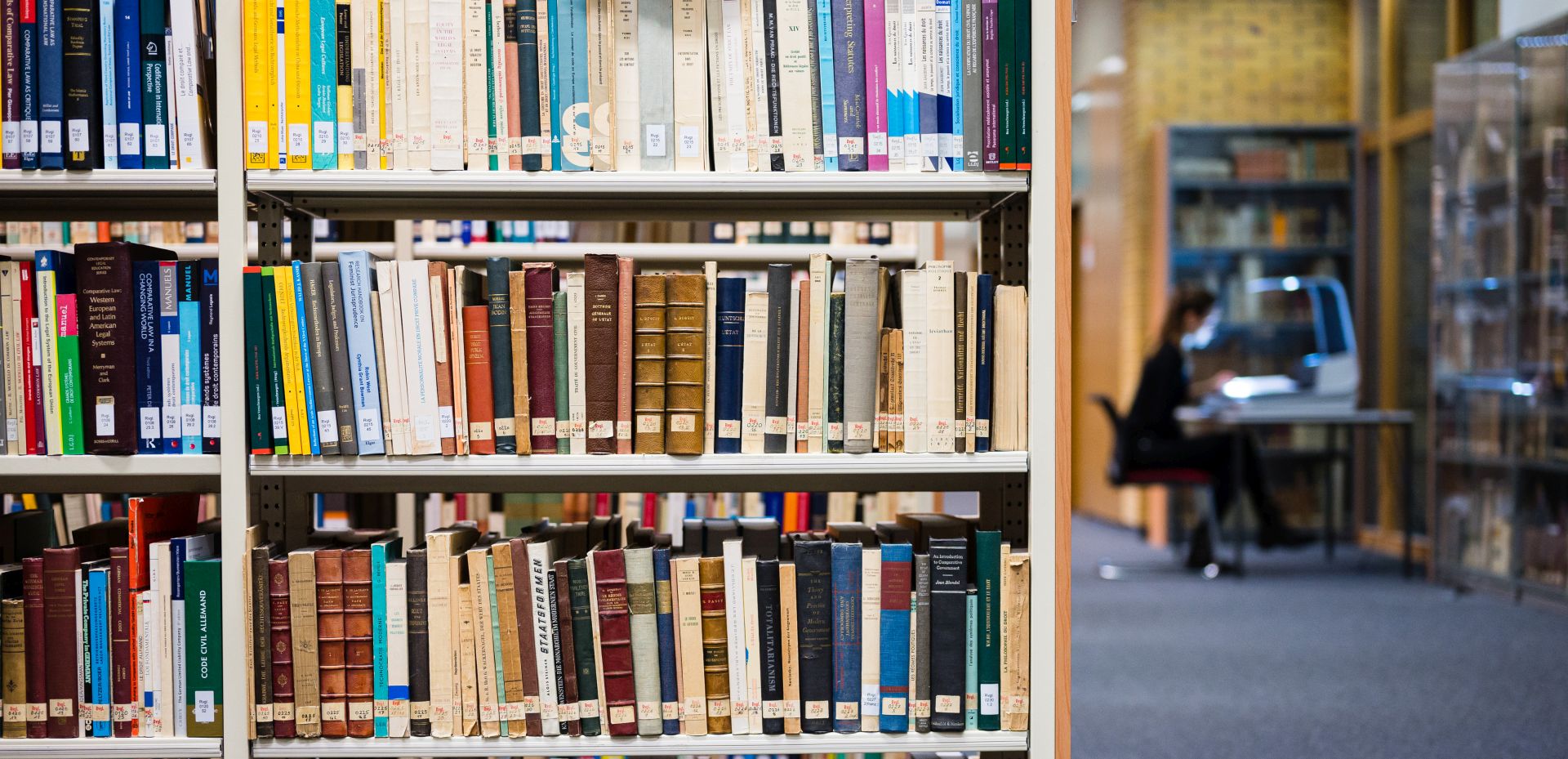 Bücherregale in einer Bibliothek mit belegtem Arbeitsplatz im Hintergrund