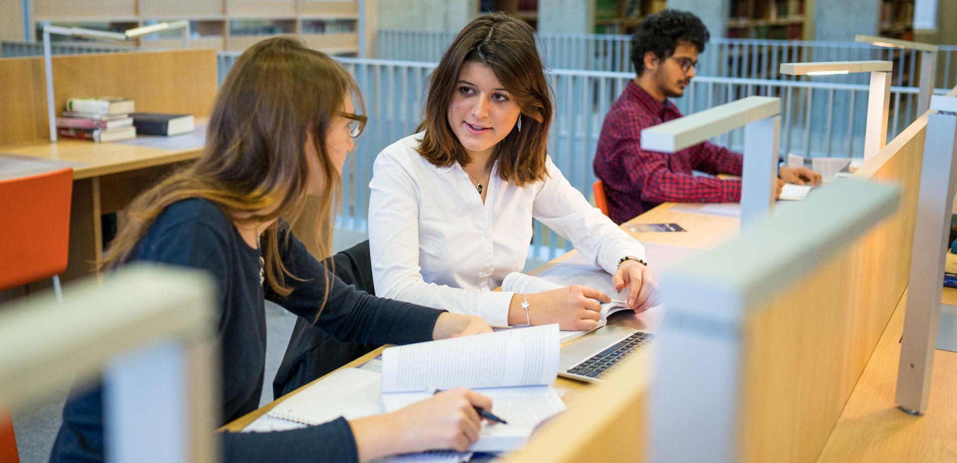 Zwei Studentinnen beraten sich am Arbeitsplatz in der Bibliothek