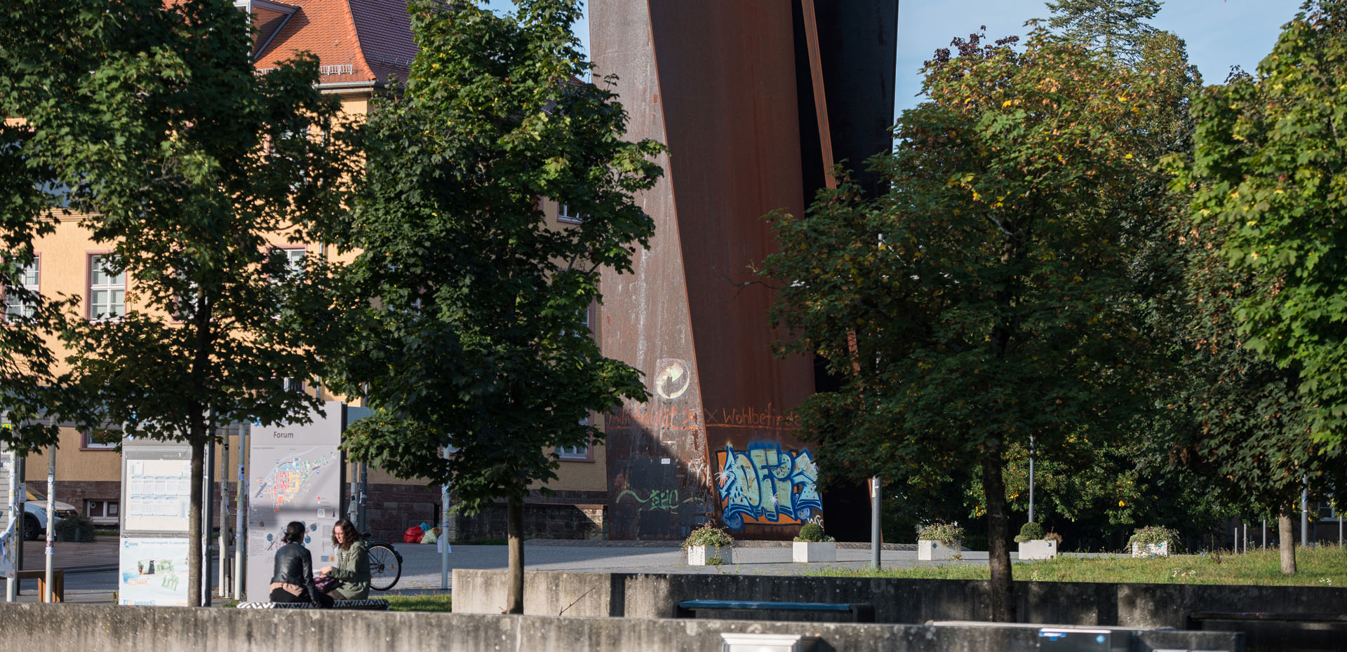 Blick durch Bäume auf die Stahlskulptur Torque von Richard Serra auf dem Campus der Universität des Saarlandes