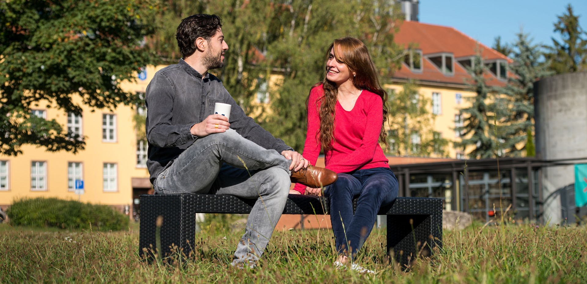 Zwei Studierende sitzen auf einer Bank in der Campuswiese