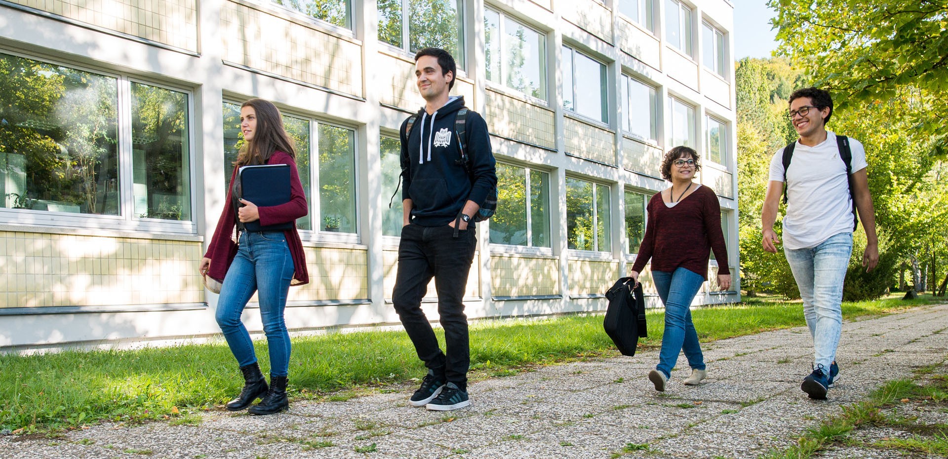 mehrere Studierende gehen einen Weg neben einem Gebäude entlang