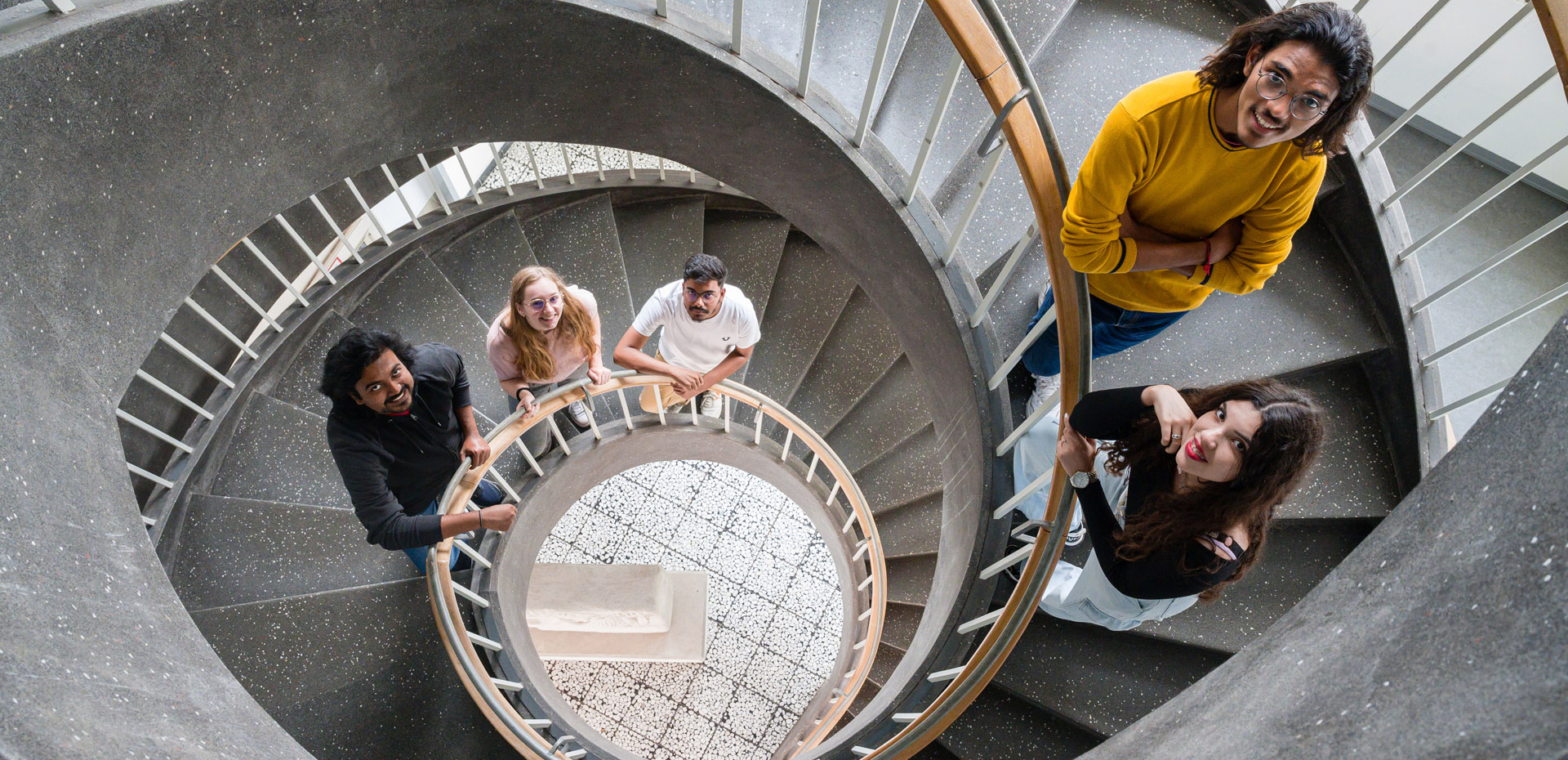 Fünf Personen auf einer geschwungenen Treppe blicken nach oben in die Kamera.