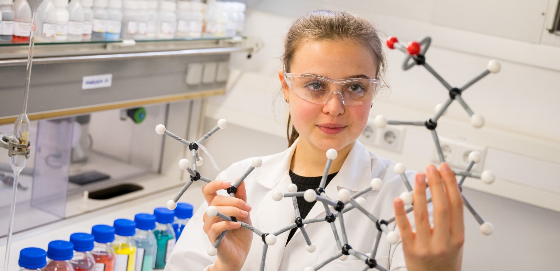 Studentin hält im Labor das Modell einer chemischen Verbindung hoch