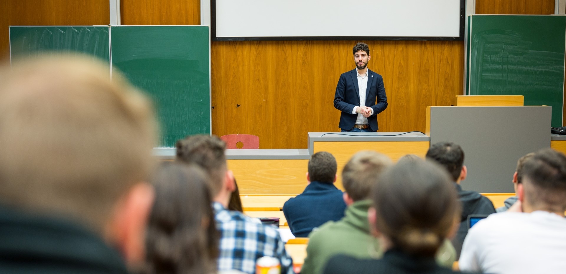 Dozent steht vor Studierenden in einem Hörsaal