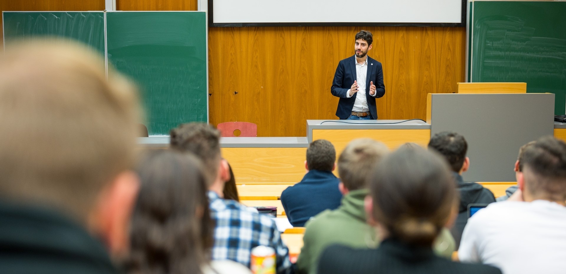 Dozent steht vor Studierenden in einem Hörsaal