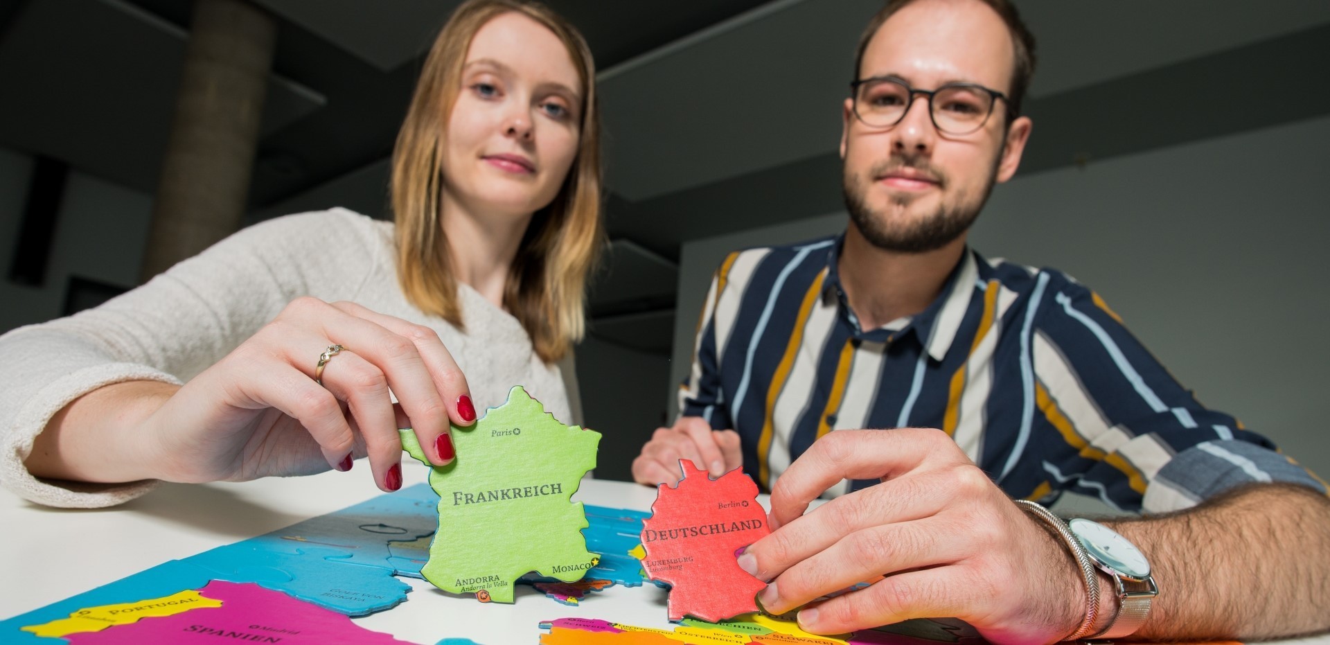 Studentin und Student zeigen zwei Puzzleteile mit dem Umriss von Frankreich und Deutschland