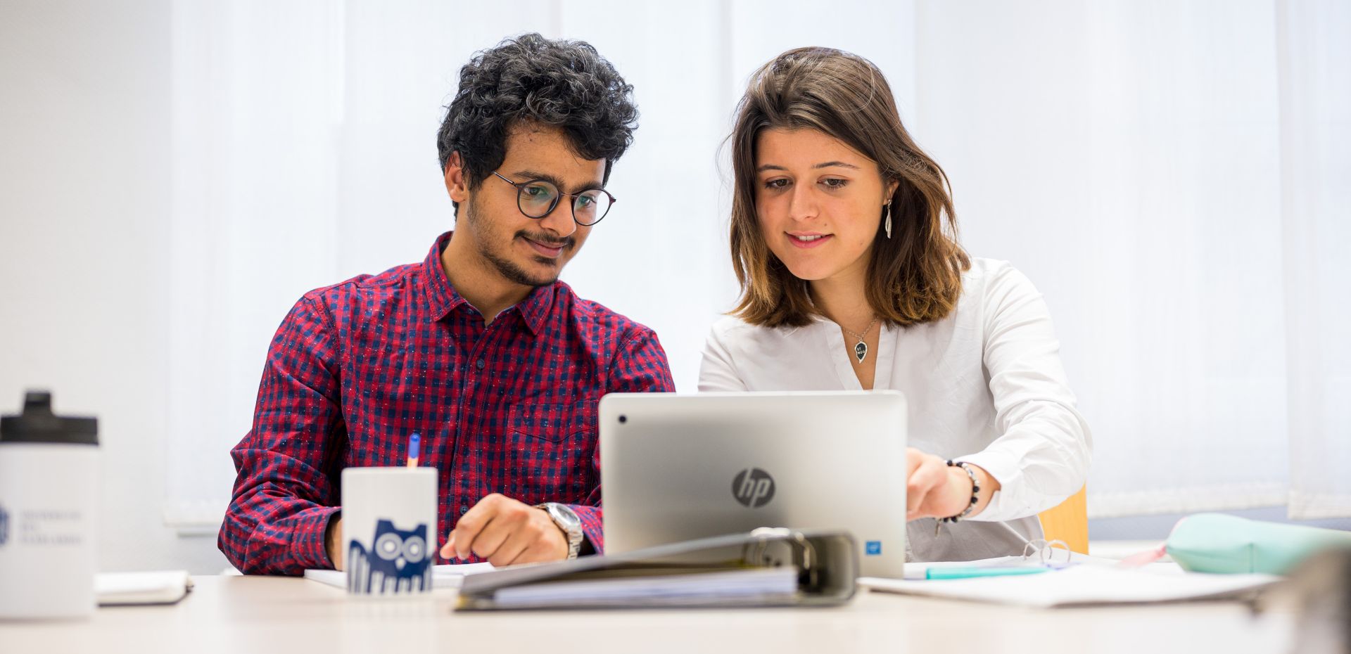 Zwei Studierende sitzen am Schreibtisch und schauen gemeinsam in einen Laptop