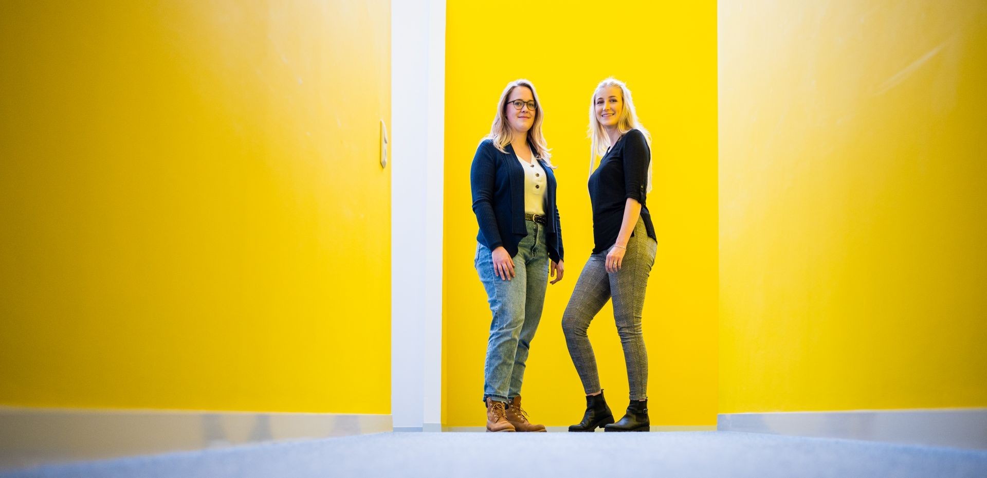 Zwei Studentinnen stehen vor einer gelben Wand