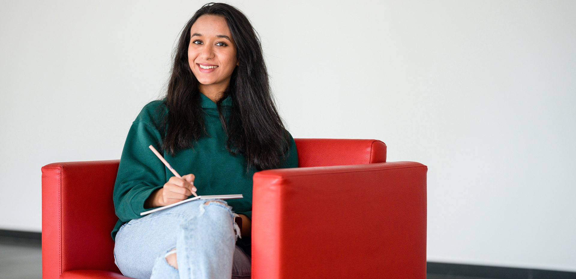 Studentin sitzt in einem roten Sessel und macht Notizen