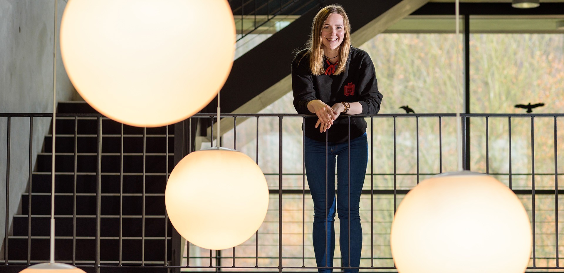 Studentin steht hinter drei Lampen auf einer Empore