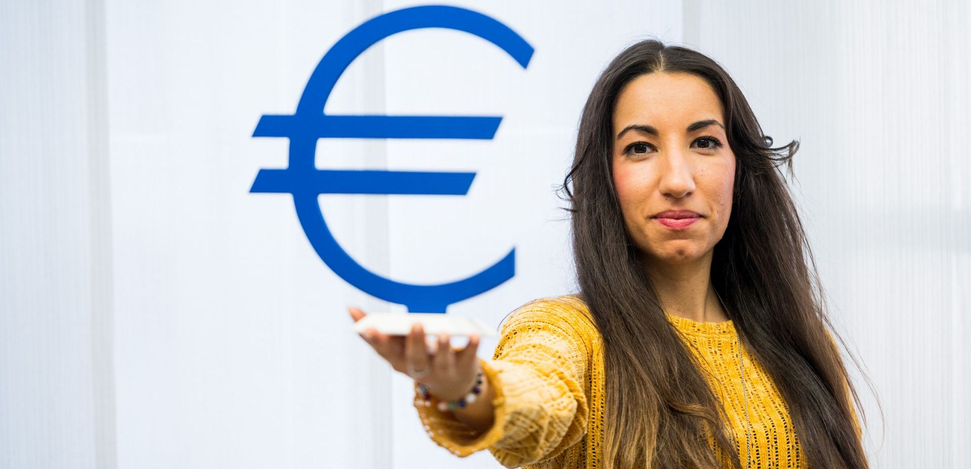 Studentin hält ein großes Euro-Symbol vor sich hoch
