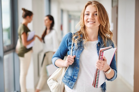 Lächelnde junge Frau steht in einem Schulflur