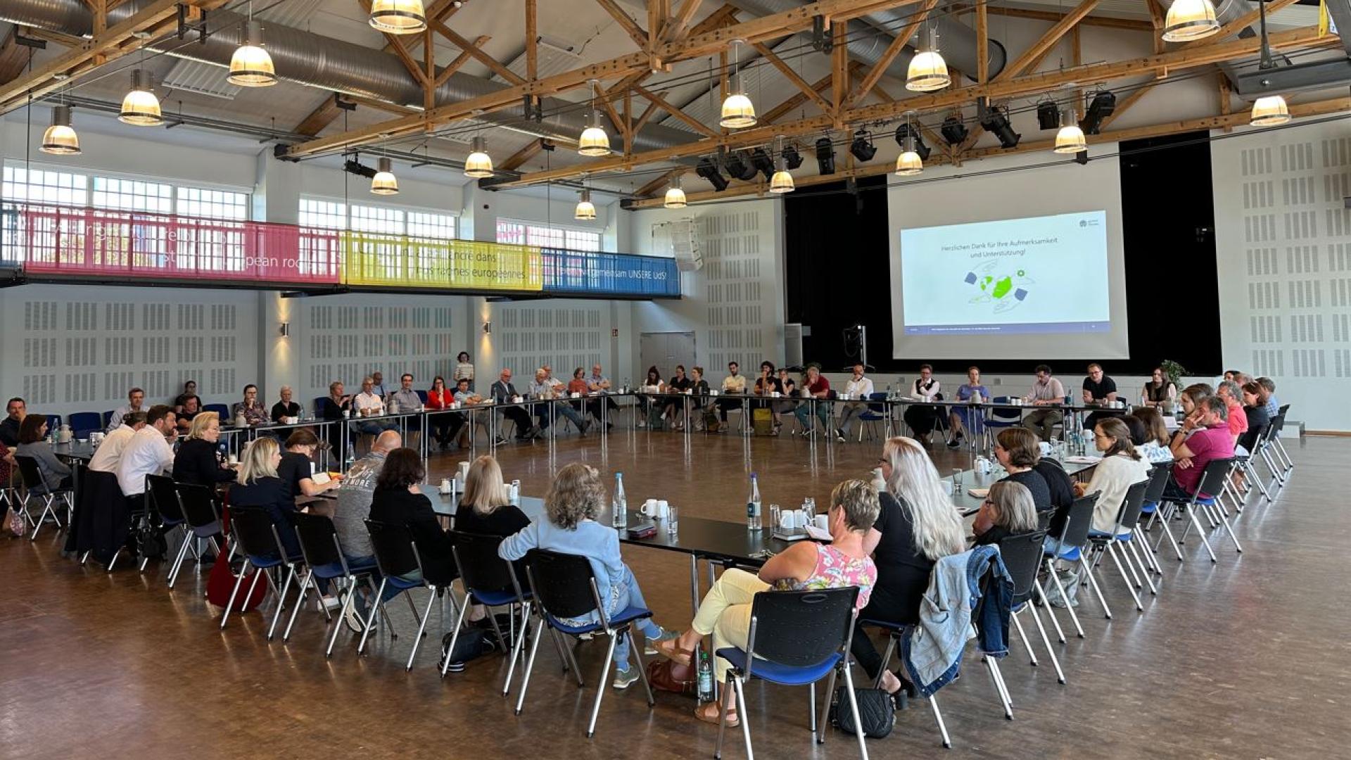 Ein Bild aus der Aula der Universität des Saarlandes auf dem 60 Personen in einem Quadrat an tischen sitzen